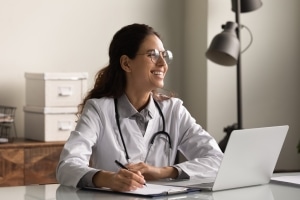 Young medical professional smiling and using a laptop