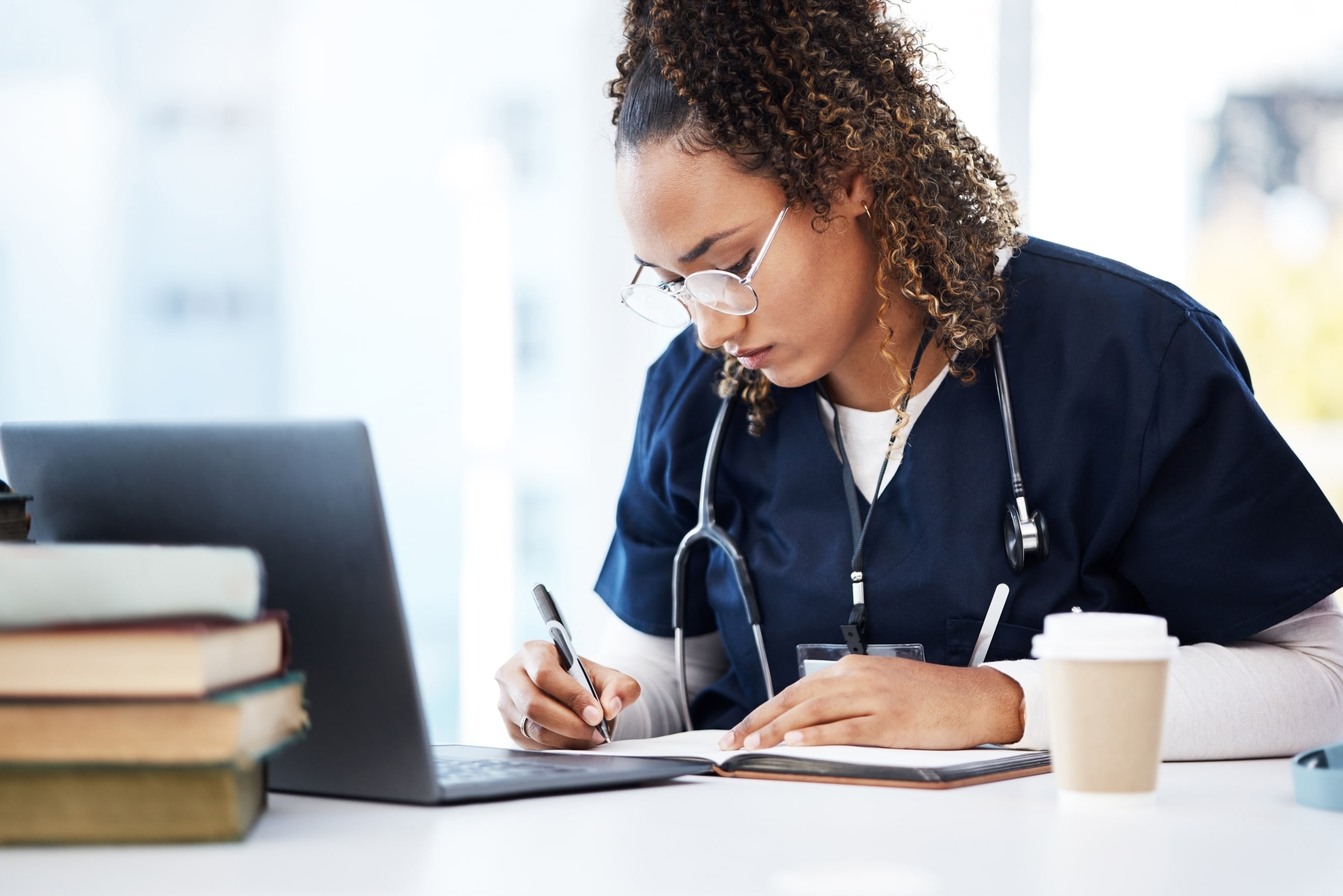 African-American nurse taking notes while using a laptop